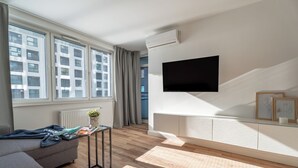 A modern living room with a grey sofa, a small table with a plant, and a mounted TV. - Pure Rental Premium Apartments (Wroclaw)