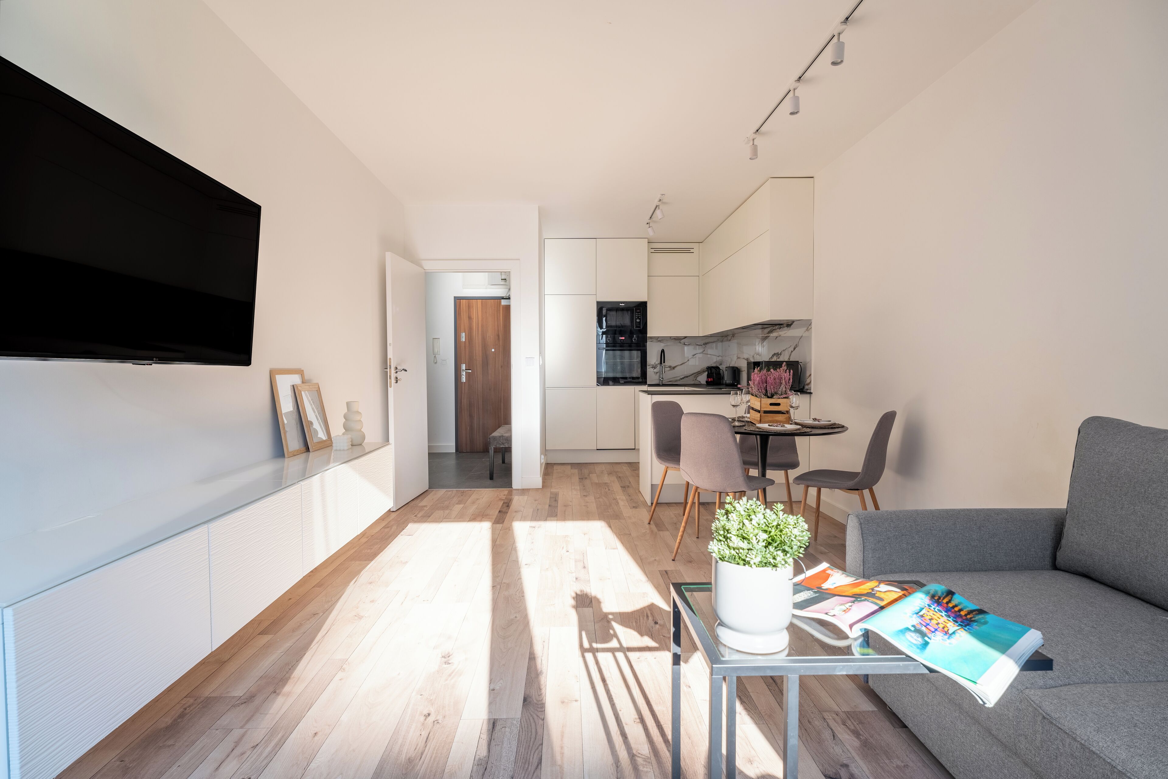 Una sala moderna con un televisor de pantalla plana, un sofá, una mesa de centro con una revista y un área de comedor con sillas y una mesa.