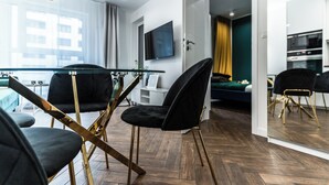A modern living room with a glass dining table, black chairs, and a flat-screen TV mounted on the wall. - Pure Rental Premium Apartments (Wroclaw)