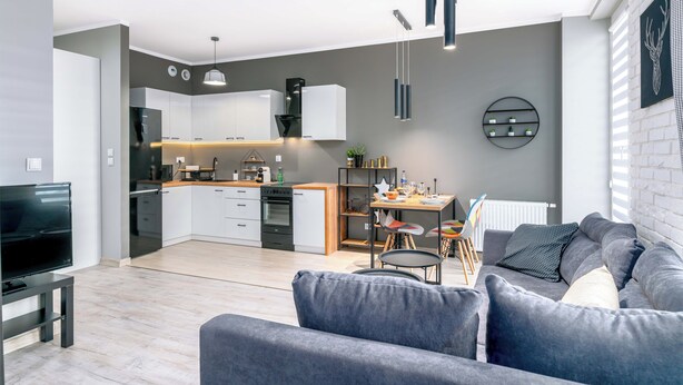A modern living room with a grey sofa, a TV, and a dining area with a table and chairs. - Pure Rental Premium Apartments (Wroclaw)