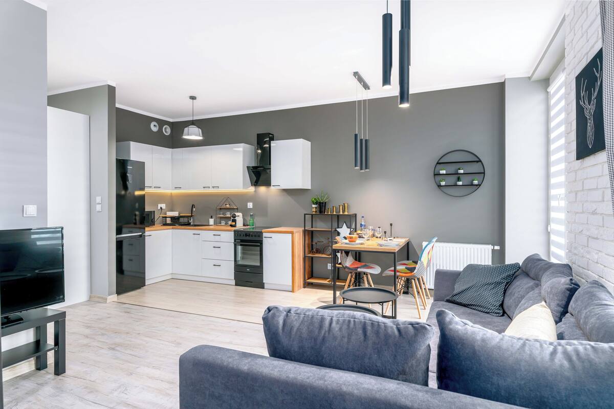 Una sala de estar moderna con un sofá gris, un televisor y un comedor con una mesa y sillas.