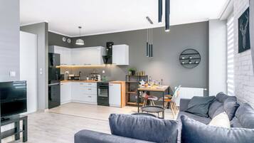 A modern living room with a grey sofa, a TV, and a dining area with a table and chairs.