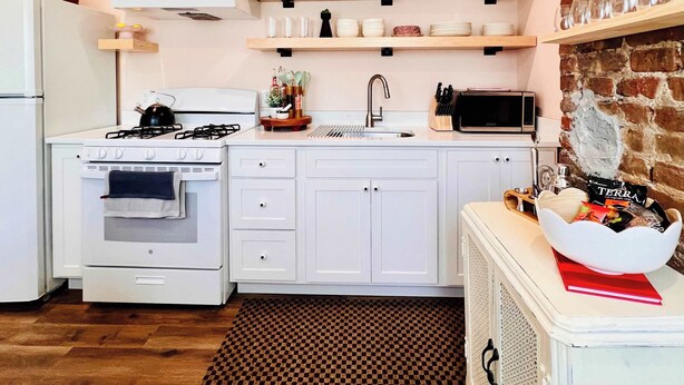 A kitchen with white cabinets, a stove, a microwave, and shelves with glassware and jars. - Mins to Stadiums - Spacious & Elegant (Pittsburgh)