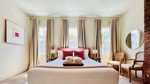 A neatly arranged hotel room with a large bed, two bedside tables, a chair, and a mirror. - Mins to Stadiums - Spacious & Elegant (Pittsburgh)