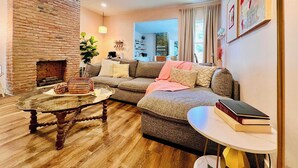 A cozy living room with a brick fireplace, a sectional sofa, a glass coffee table, and a small round table with books. - Mins to Stadiums - Spacious & Elegant (Pittsburgh)