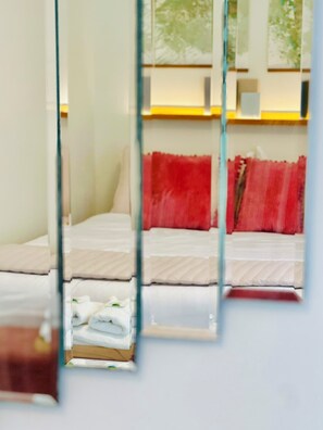 A hotel room with a bed, a red pillow, and a window with a view of trees.