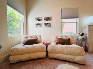 Una habitación con dos sillones tapizados, un pequeño taburete rosa y un mueble con cajones. Hay cuatro fotografías blanco y negro en la pared.