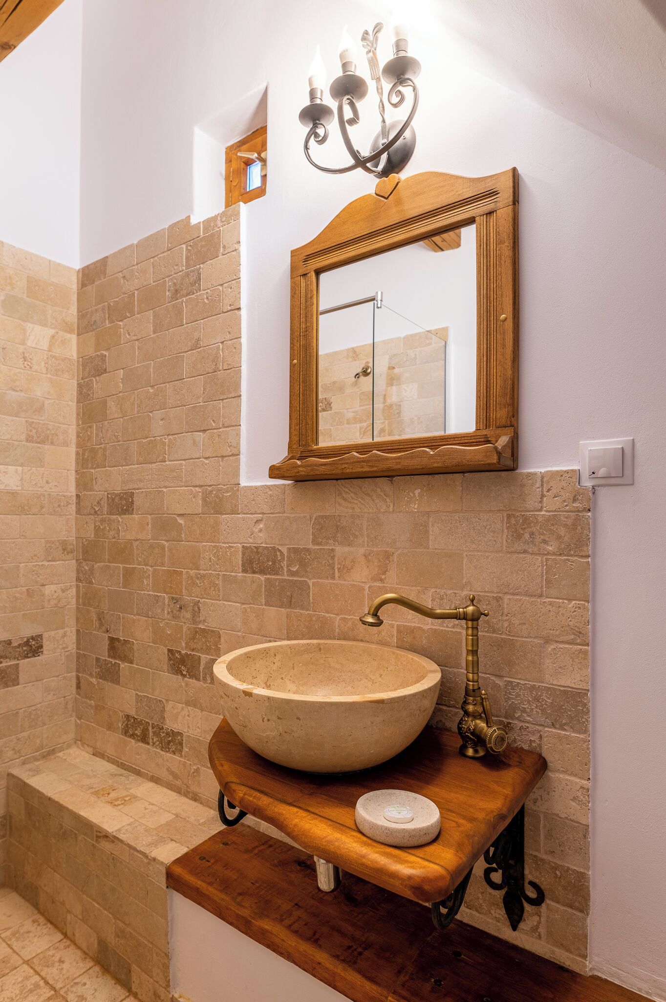 A bathroom with a large, round sink on a wooden countertop, a mirror above it, and a chandelier.