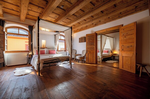 A wooden-floored bedroom with a four-poster bed, a window with curtains, a radiator, and a small table with a lamp. - Boutique Hotel von Graf (Sighisoara)