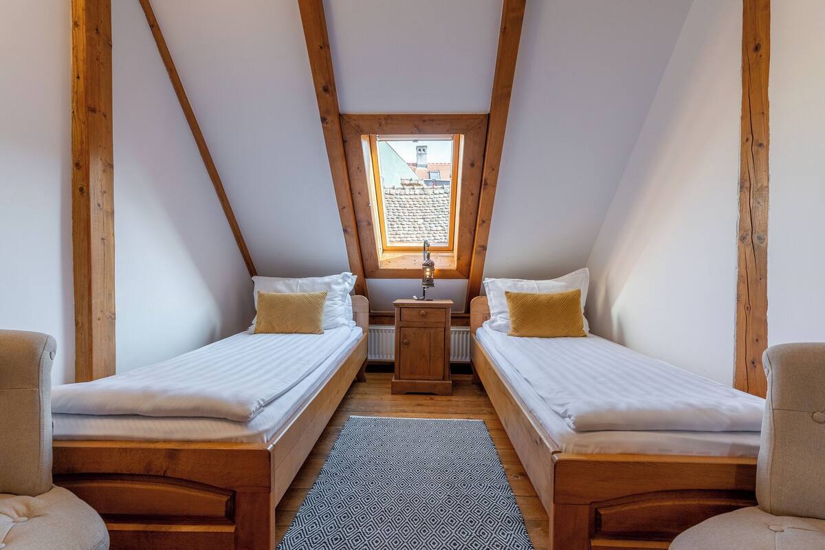 A small, cozy room with two wooden beds, a small table, and a window with a view of buildings.