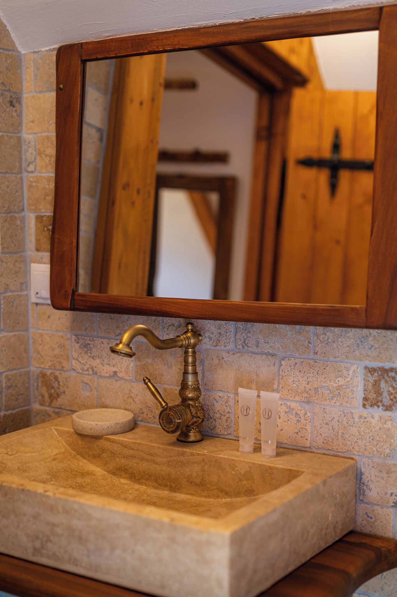 A bathroom with a stone sink, wooden frame mirror, and a towel dispenser.