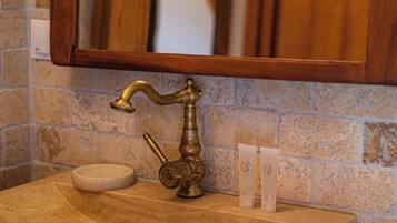 A bathroom with a stone sink, wooden frame mirror, and a towel dispenser.