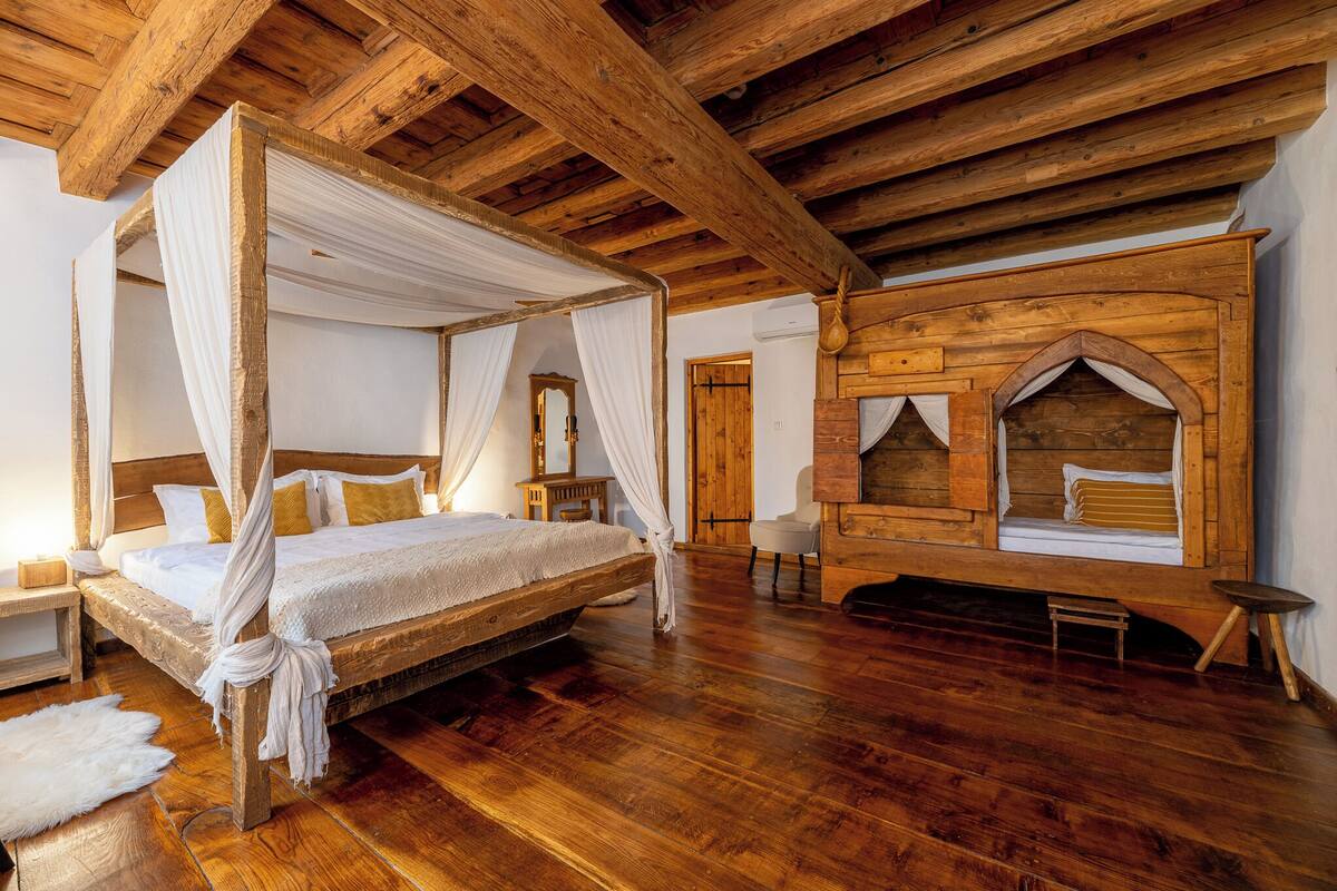 A four-poster bed with a canopy, wooden flooring, and a rustic wooden wall with a built-in bench.