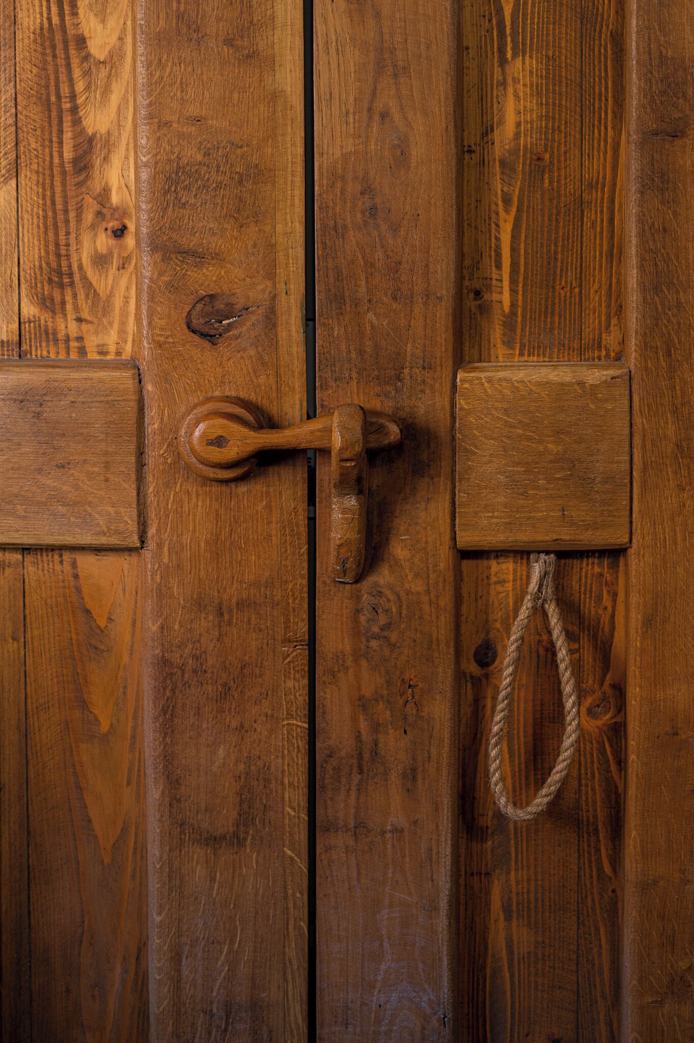 Una puerta de madera con un cerrojo metálico y un tirador de cuerda.