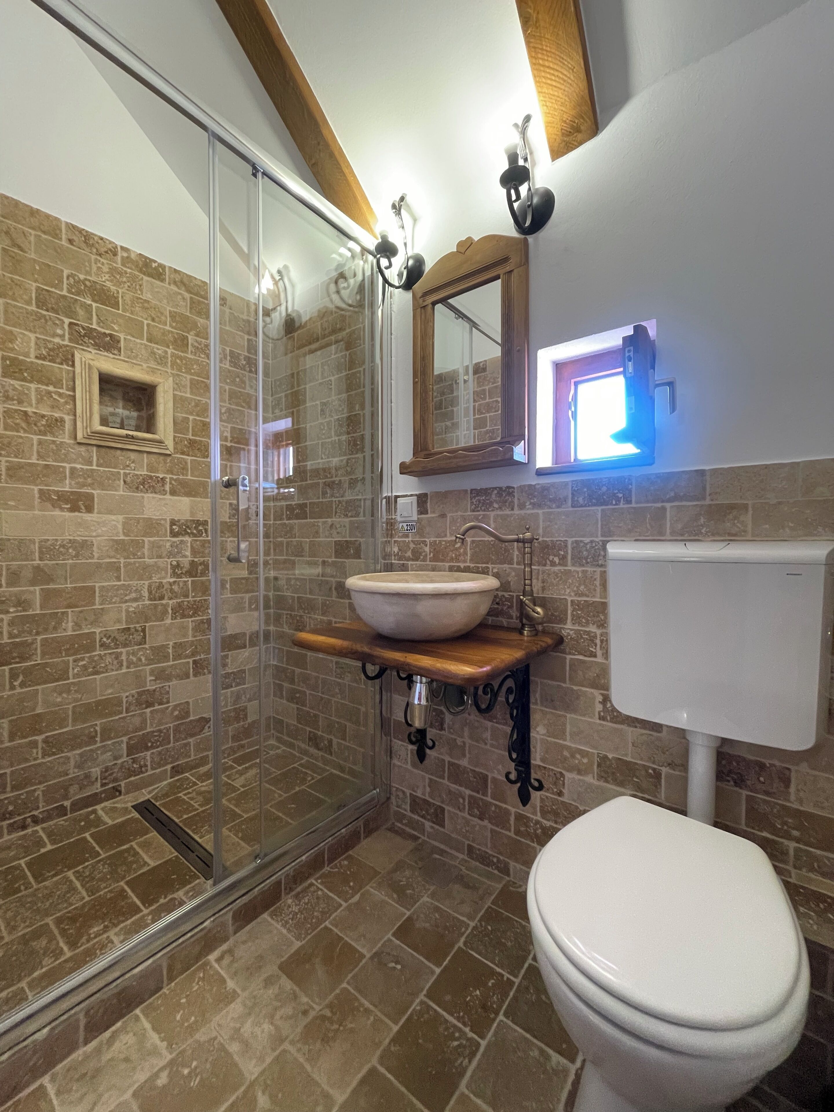 A bathroom with a glass shower enclosure, a wooden vanity with a bowl sink, a toilet, and a mirror with integrated lighting.