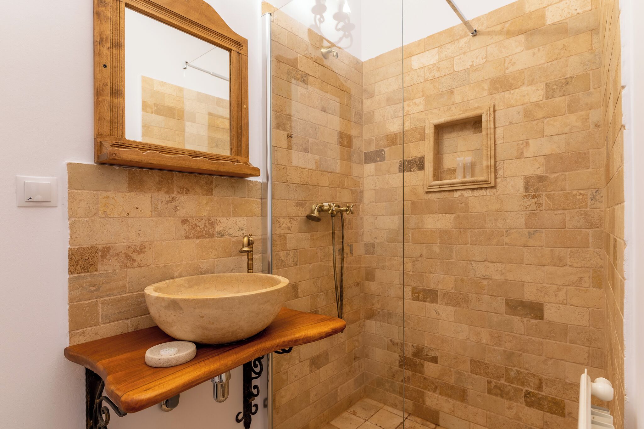 A bathroom with a stone sink, wooden countertop, and a shower with beige tiles.