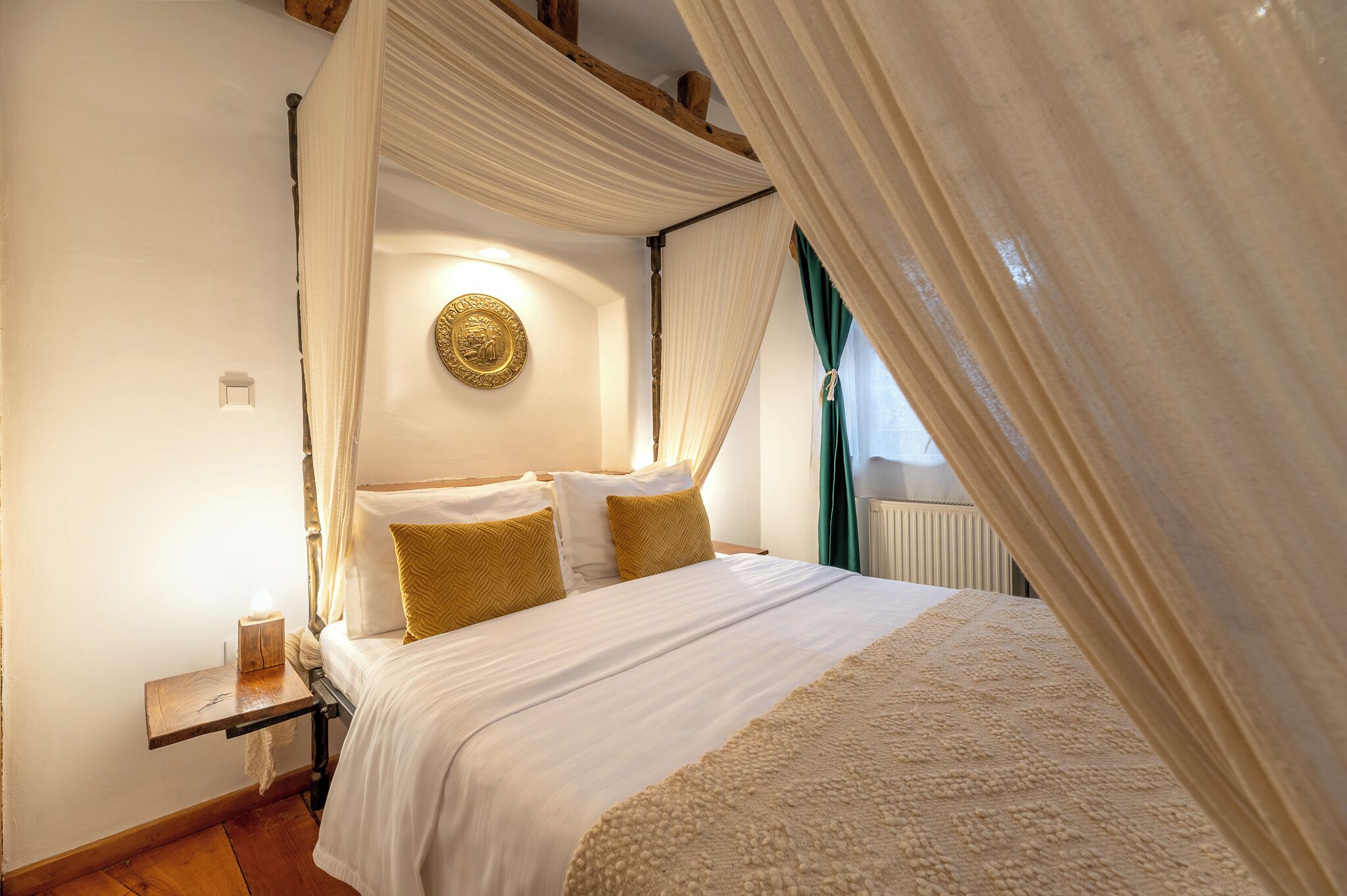 A bedroom with a four-poster bed, a bedside table with a lamp, and a decorative wall plate.