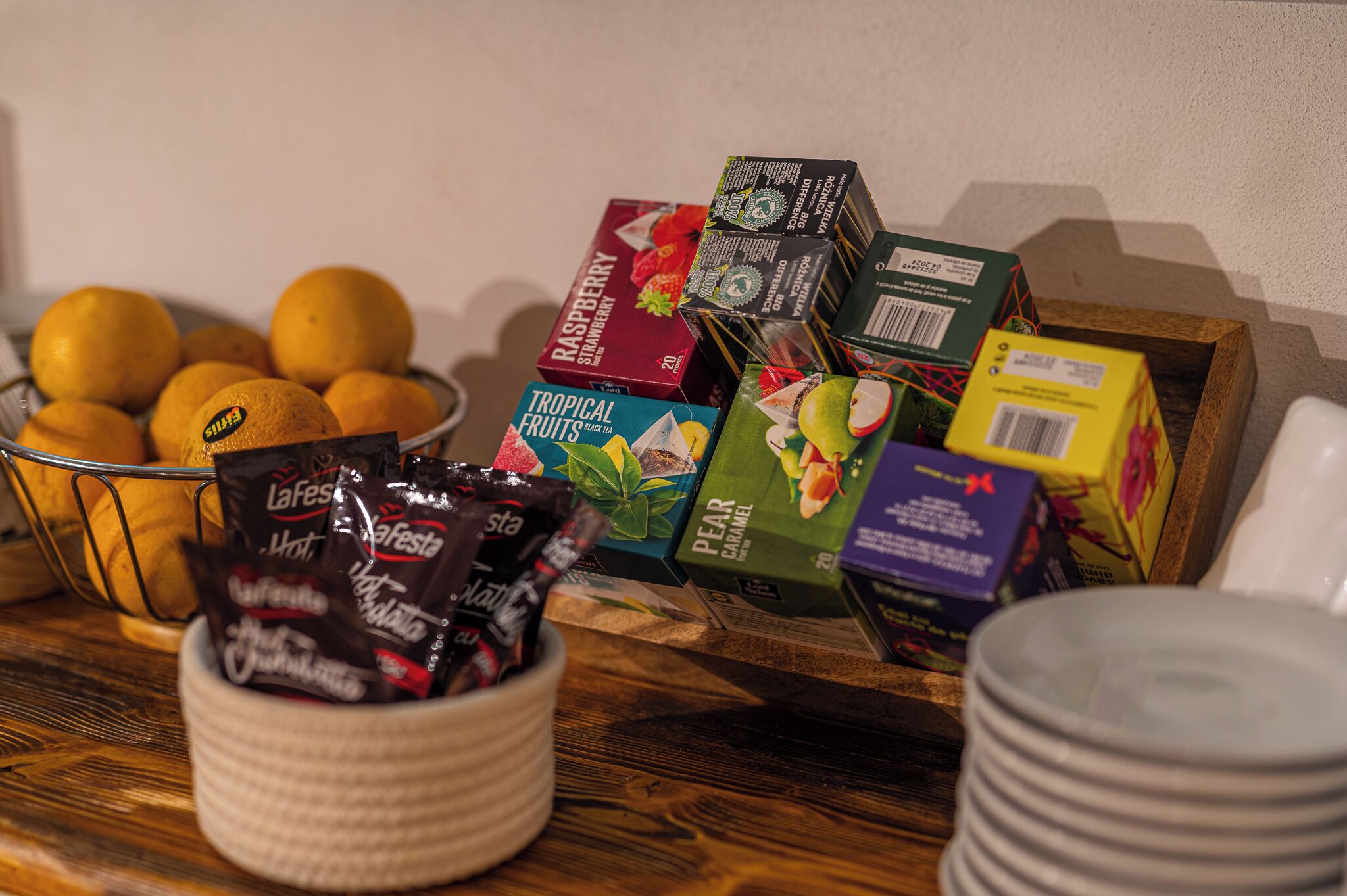 A table with a fruit bowl, a basket of chocolate, and several boxes of fruit-flavored drinks.