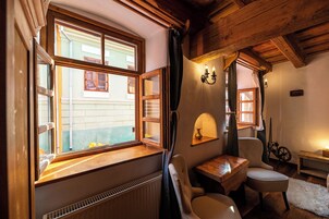 Una habitación acogedora con techo de madera, una ventana con cortinas, una mesita, una silla y un radiador.