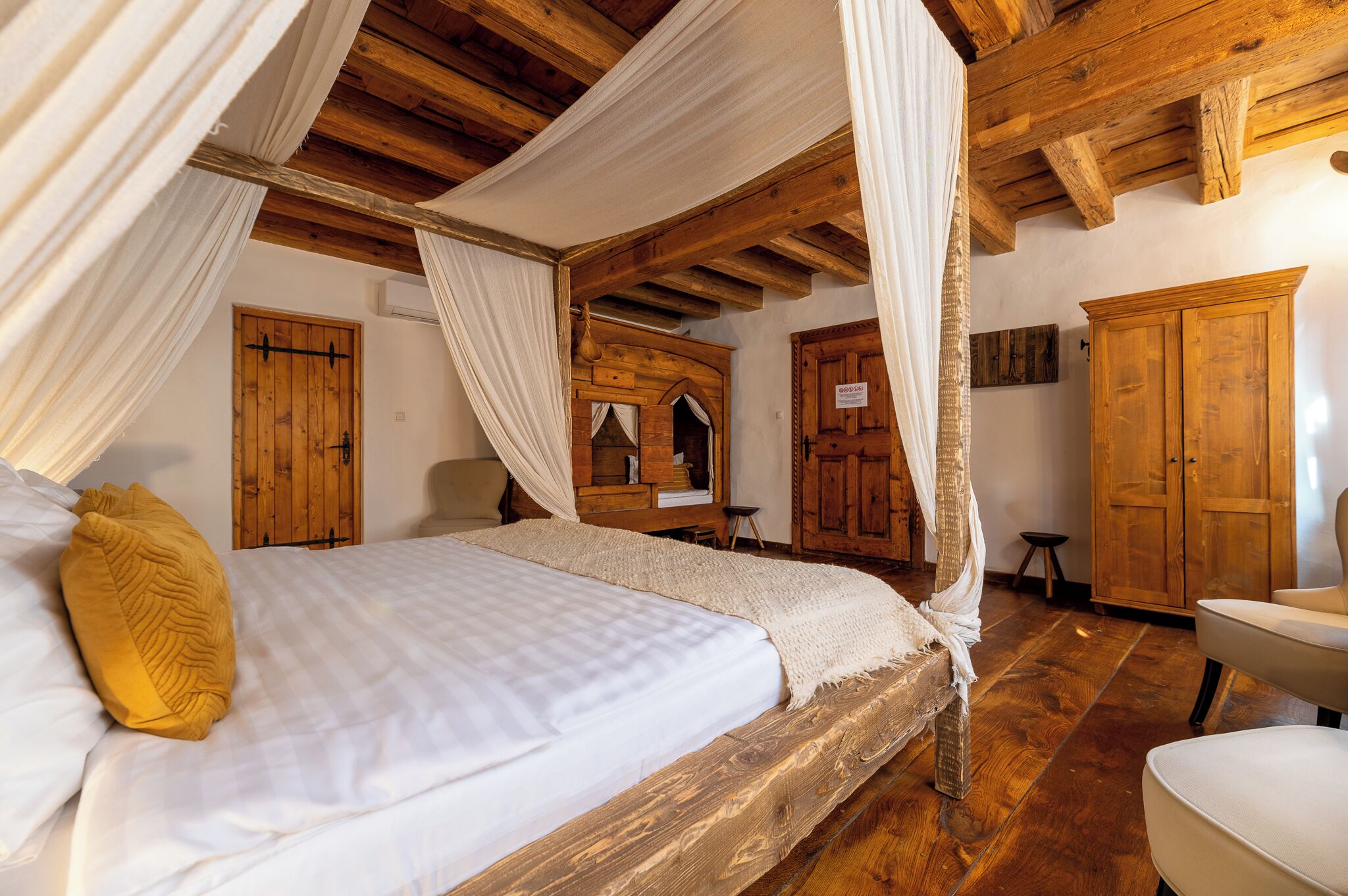 Una stanza con un letto di legno, tende bianche e un armadio in legno.