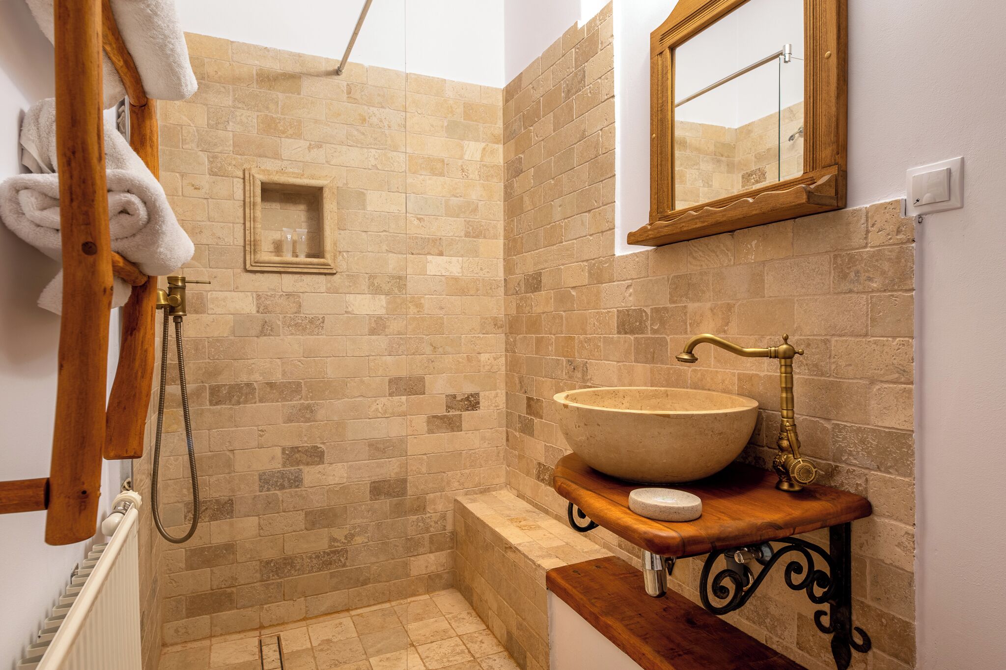 A bathroom with a stone-tiled shower, a wooden vanity with a large basin, and a small mirror above the sink.