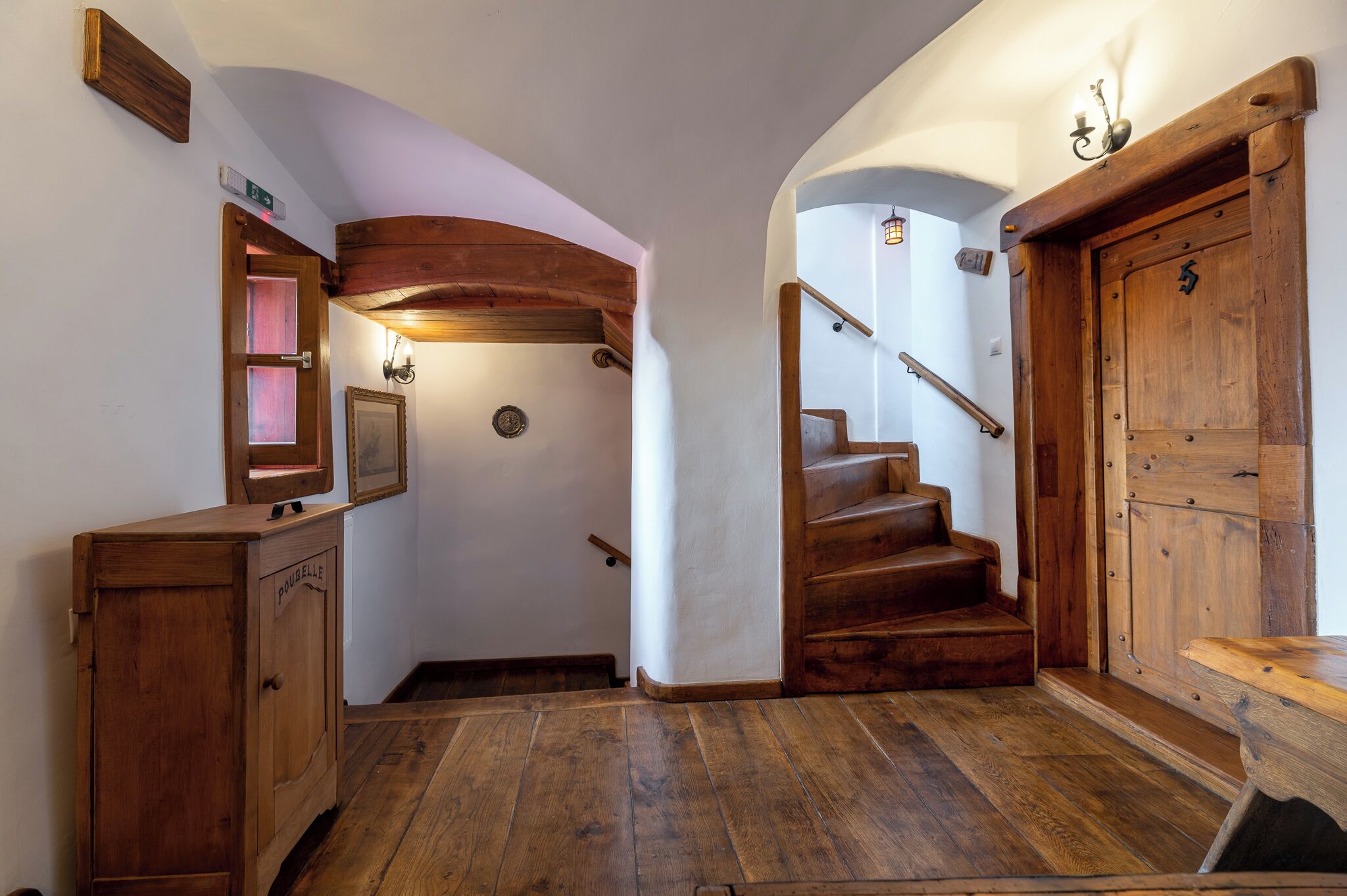 A wooden staircase with a handrail, a wooden cabinet with a glass door, and a wall-mounted light fixture.