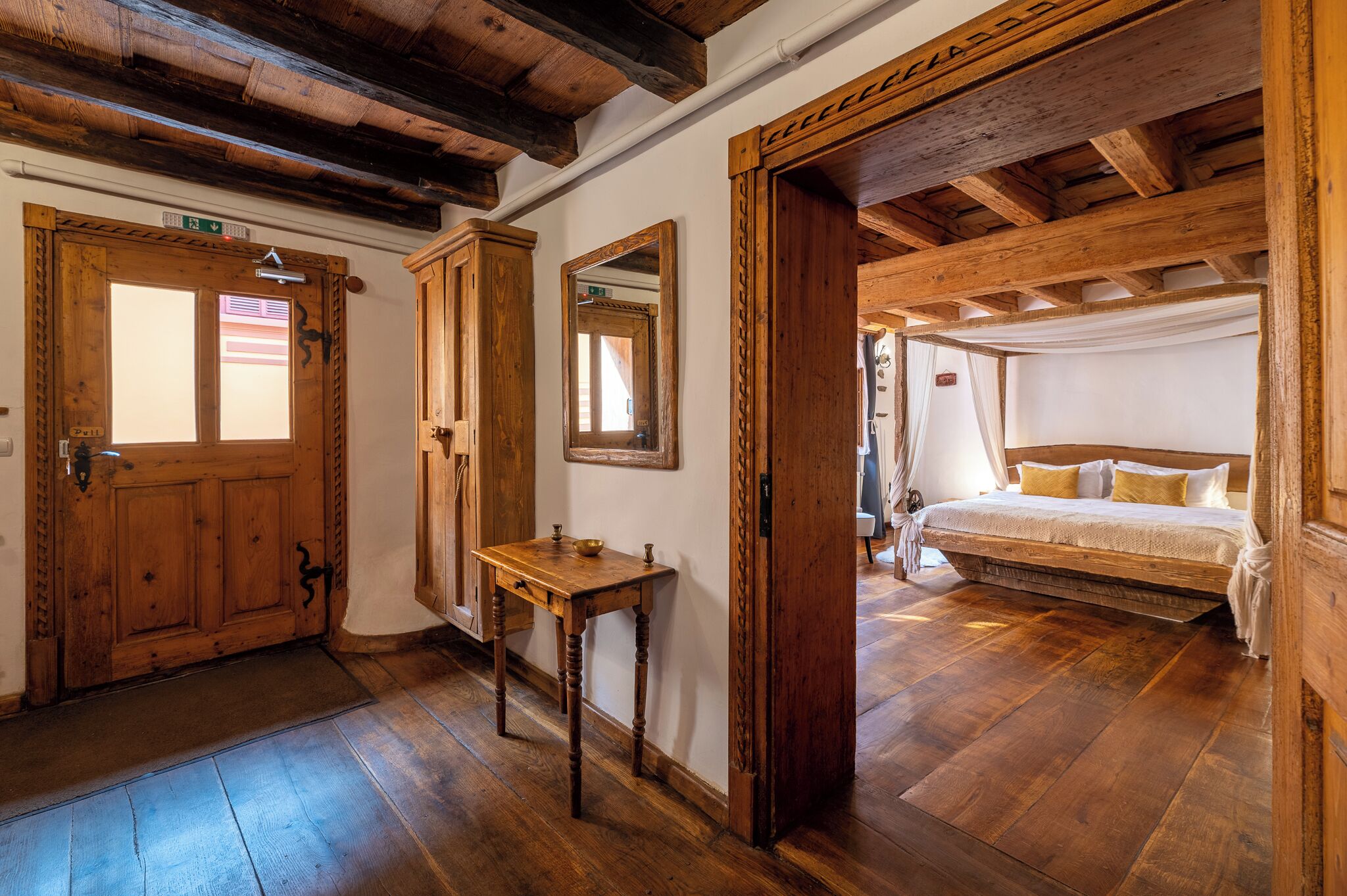 Una habitación con suelo de madera, una cama, una mesa de madera y un espejo.