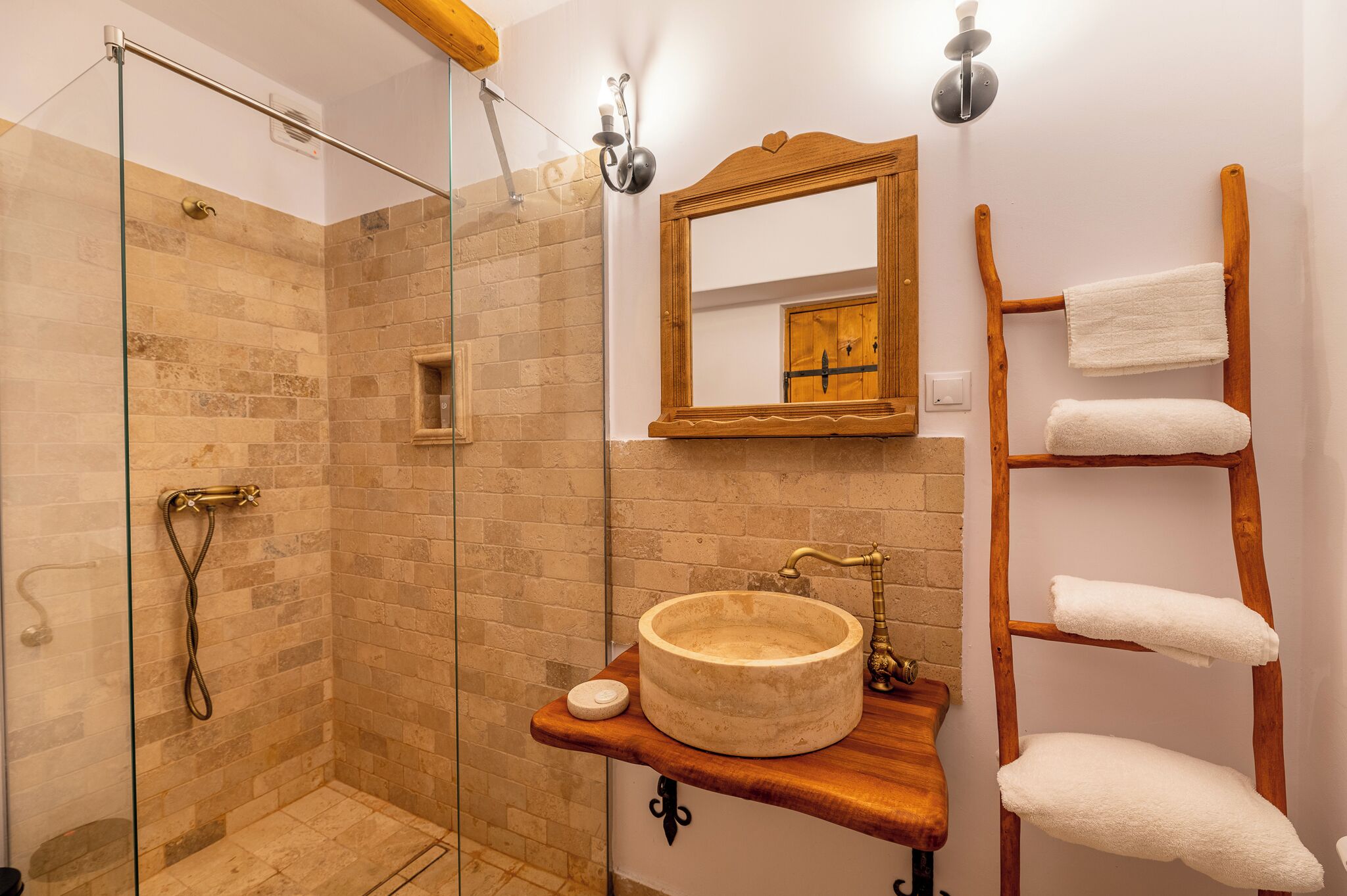 Un bagno con doccia vetrata, un mobile contenitore in legno con lavabo tondo e un portasciugamani in legno.