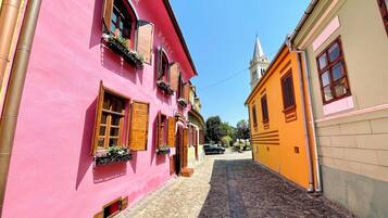 A narrow cobblestone street lined with colorful buildings, including a pink building with wooden shutters and a yellow building with a bell tower.