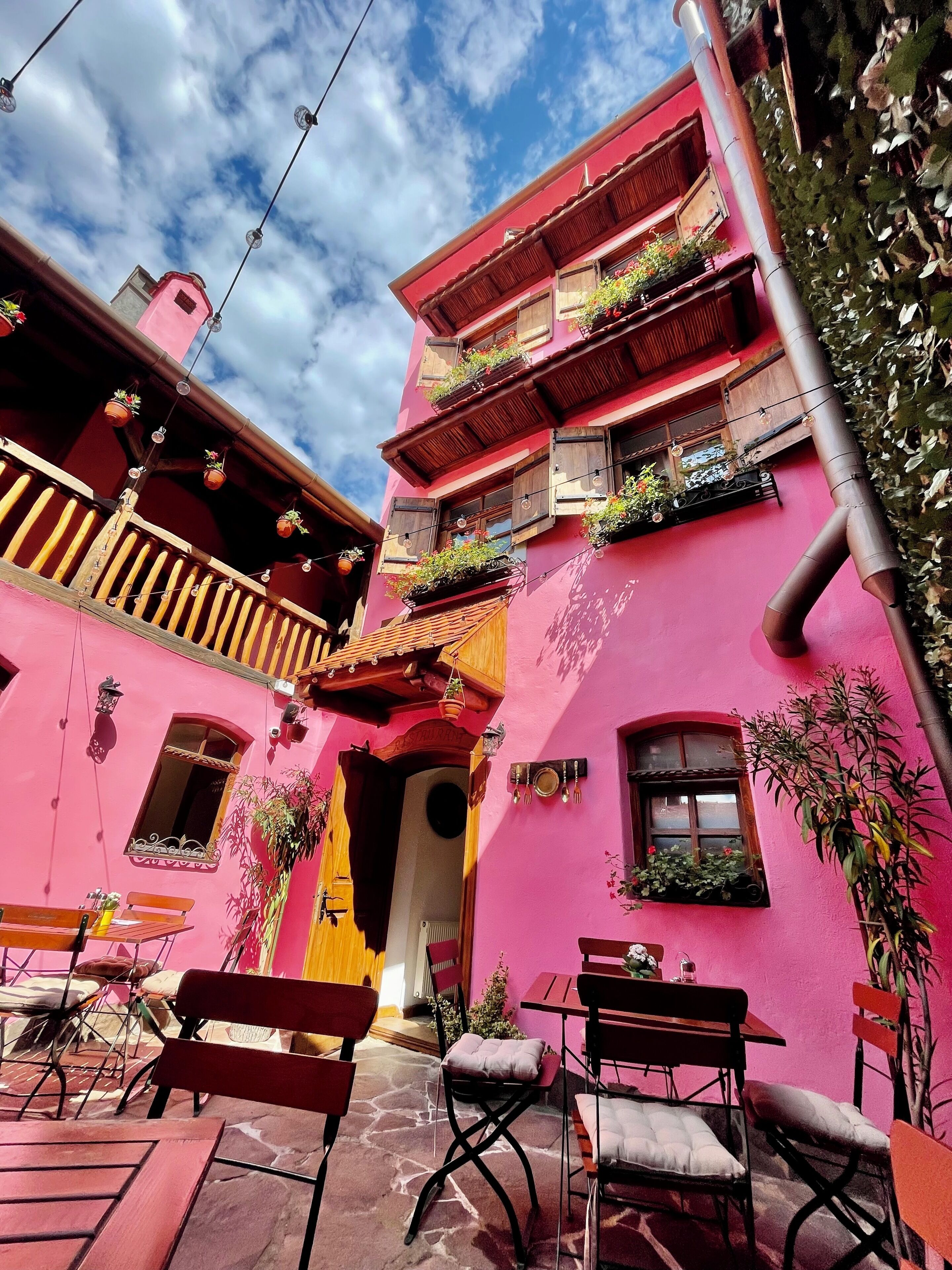 A narrow street with pink buildings, outdoor seating, and hanging plants.