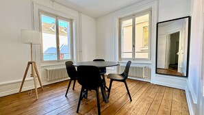 A room with a wooden floor, white walls, a round table with four chairs, a floor lamp, and large windows with a view of buildings. - Cozy & Fully Equipped 2-Bedroom Apartment in Central Zurich (Zürich)