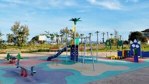 A playground with various play structures, including a slide and swings, set on a paved area with a clear sky above. - Villa Particular, Confortable (VC)
