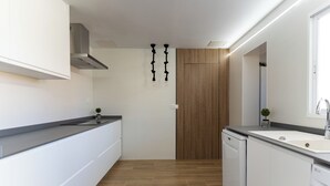 A modern kitchen with white cabinetry, a wooden accent wall, and a built-in dishwasher. - Villa Particular, Confortable (VC)