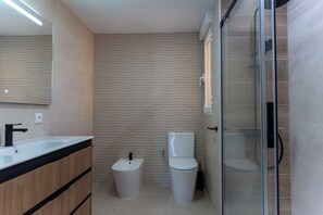 A modern bathroom with a wooden vanity, a bidet, a toilet, and a glass-enclosed shower area.