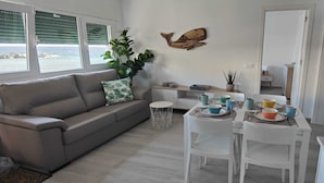Una sala de estar moderna con un sofá gris, una mesa de comedor con cuencos y tazas de colores, una planta en maceta y un adorno de pared de madera.