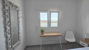 Una habitación pequeña y limpia con escritorio, silla y ventana con vista al mar.