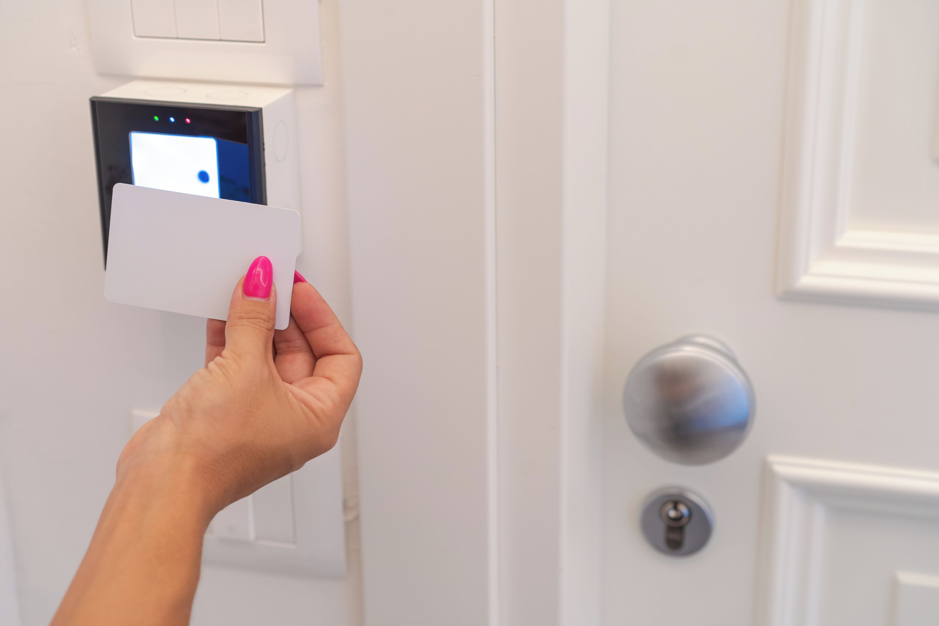 A hand holding a card in front of a door with a digital lock and a keyhole.
