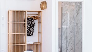 Habitación con armario de madera, perchero con ropa, ducha con paredes de mármol y cama blanca.