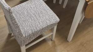 A dining table with a woven placemat, two upholstered chairs, and a small side table with condiments.