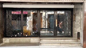 Facciata di un edificio con cancelli in metallo decorati, un ingresso in pietra e un cartello che indica la sicurezza.