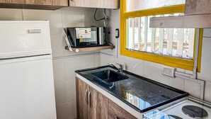Una cucina compatta con frigorifero, microonde, lavello e fornello.