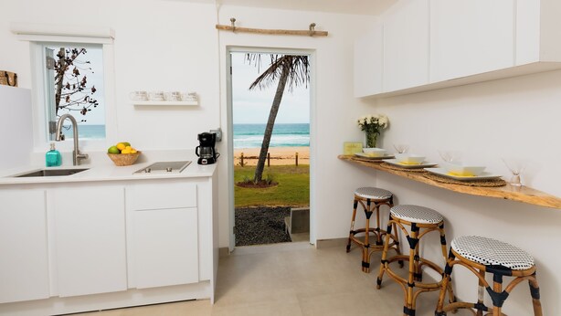 Una cucina con vista sulla spiaggia, caratterizzata da mobili bianchi, una macchina da caffè e una ciotola di frutta.
