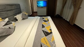 A hotel room with a large bed, a flat-screen TV mounted on the wall, and a wooden door. - Wellaton Suite (Abuja)