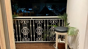 A balcony with a metal railing, a potted plant, and a stool. - Wellaton Suite (Abuja)