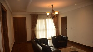 A living room with a sofa, a chair, a chandelier, and a door. - Wellaton Suite (Abuja)