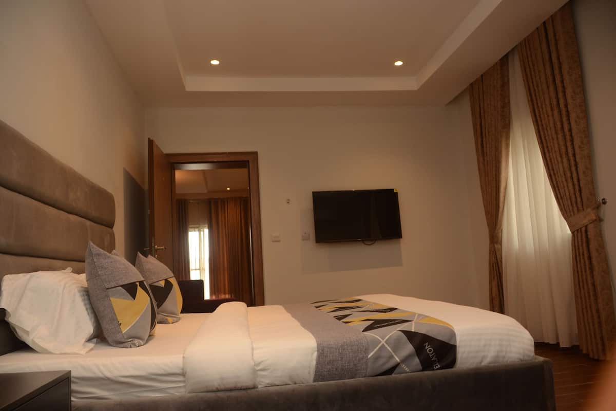 A modern hotel room with a large bed, a flat-screen TV, and a view of the hallway.