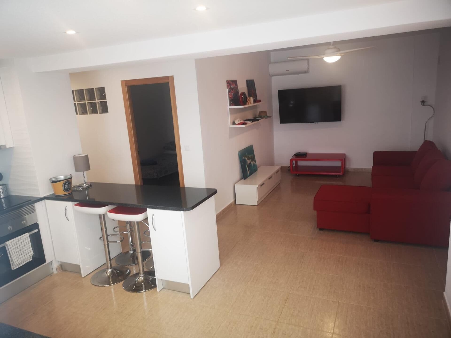 A modern kitchen with a dining area, a red sofa, and a flat-screen TV mounted on the wall.
