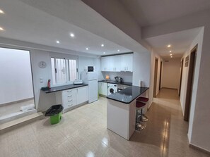 A modern kitchen with white cabinets, a black countertop, and a small island with stools. - Luxurious Villa La Vita e Bella Escape in Murcia (Murcia)