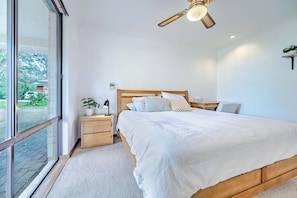 Un dormitorio con una cama grande, una mesita de noche, un ventilador de techo y una ventana con vistas al exterior.