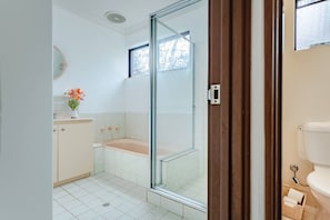 Un baño con cabina de ducha de vidrio, inodoro y lavamanos con un florero.